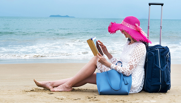 Frau sitzt am Strand und hält ein iPad in der Hand